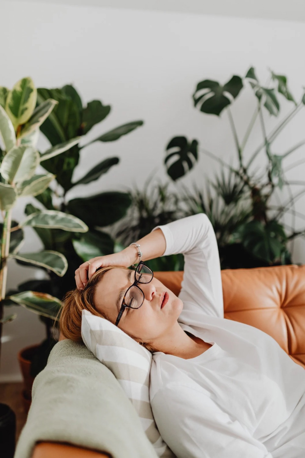 tired woman lying on a sofa with a pillow and blanket under her head and some house plants in the background
