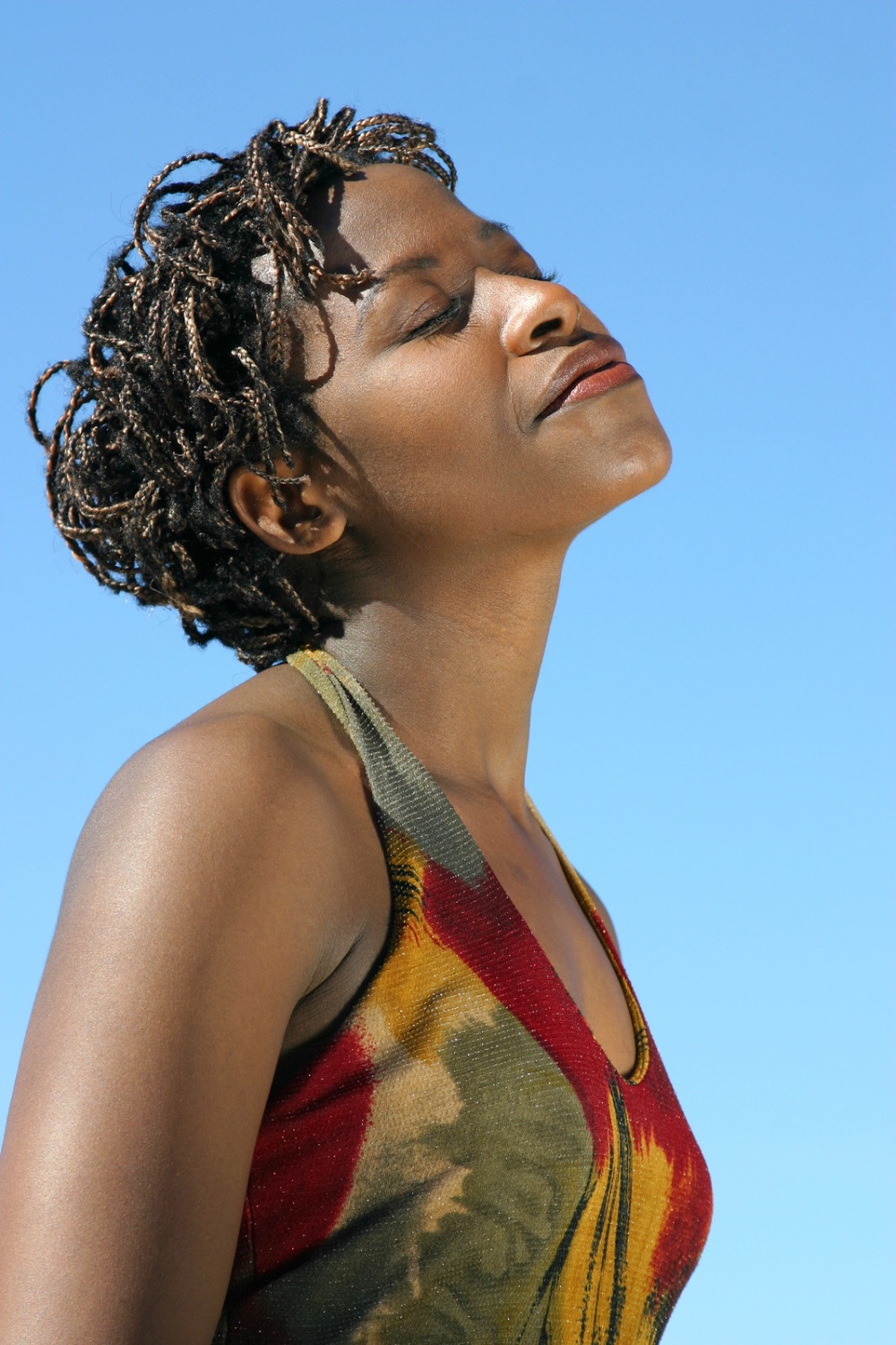 Woman with closed eyes and head tilted up towards the sky, with a blue sky in the background, representing well-being