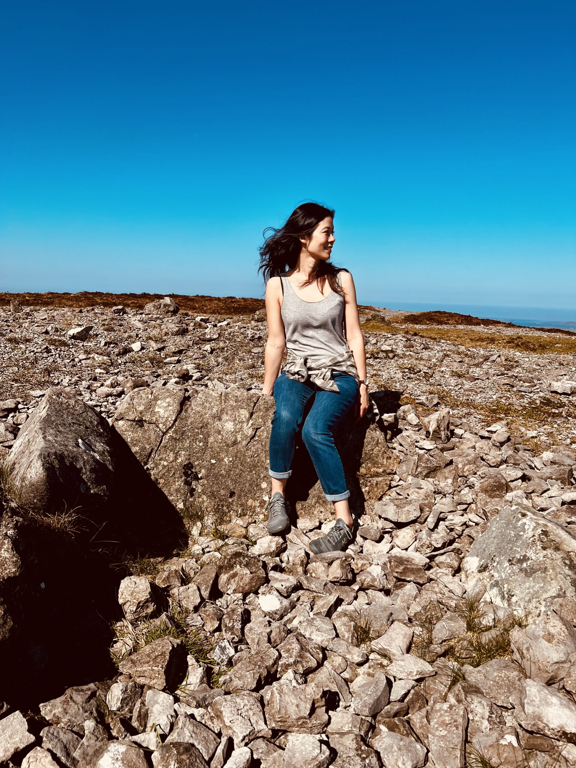 Woman sitting on a rock at the top of a mountain looking to the side, with a very blue sky in the background