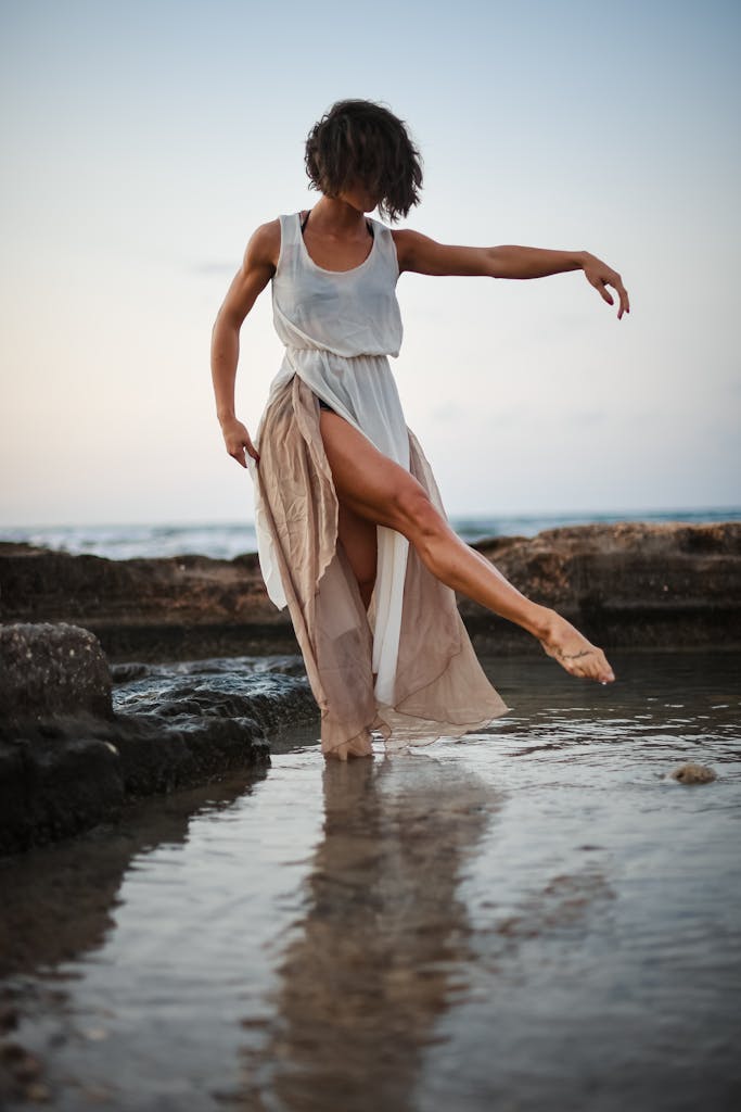 A woman dances gracefully by the seashore at Polignano A Mare, Italy, barefoot and in flowing dress.