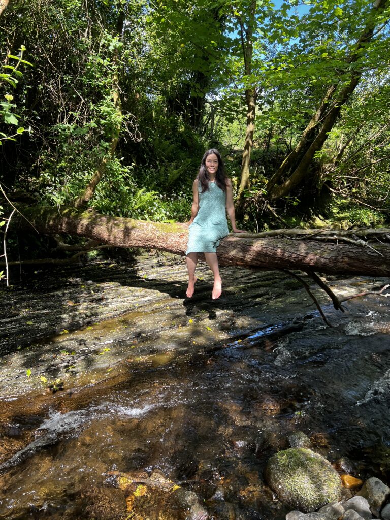 woman sitting on a tree trunk above a river in a forest