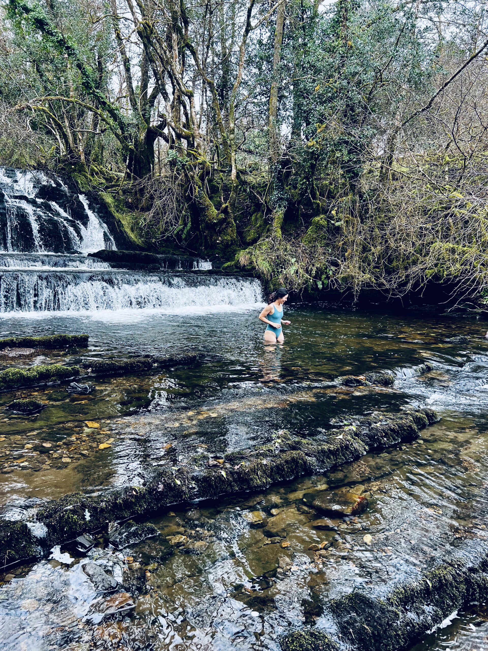 woman standing in a river below a waterfall