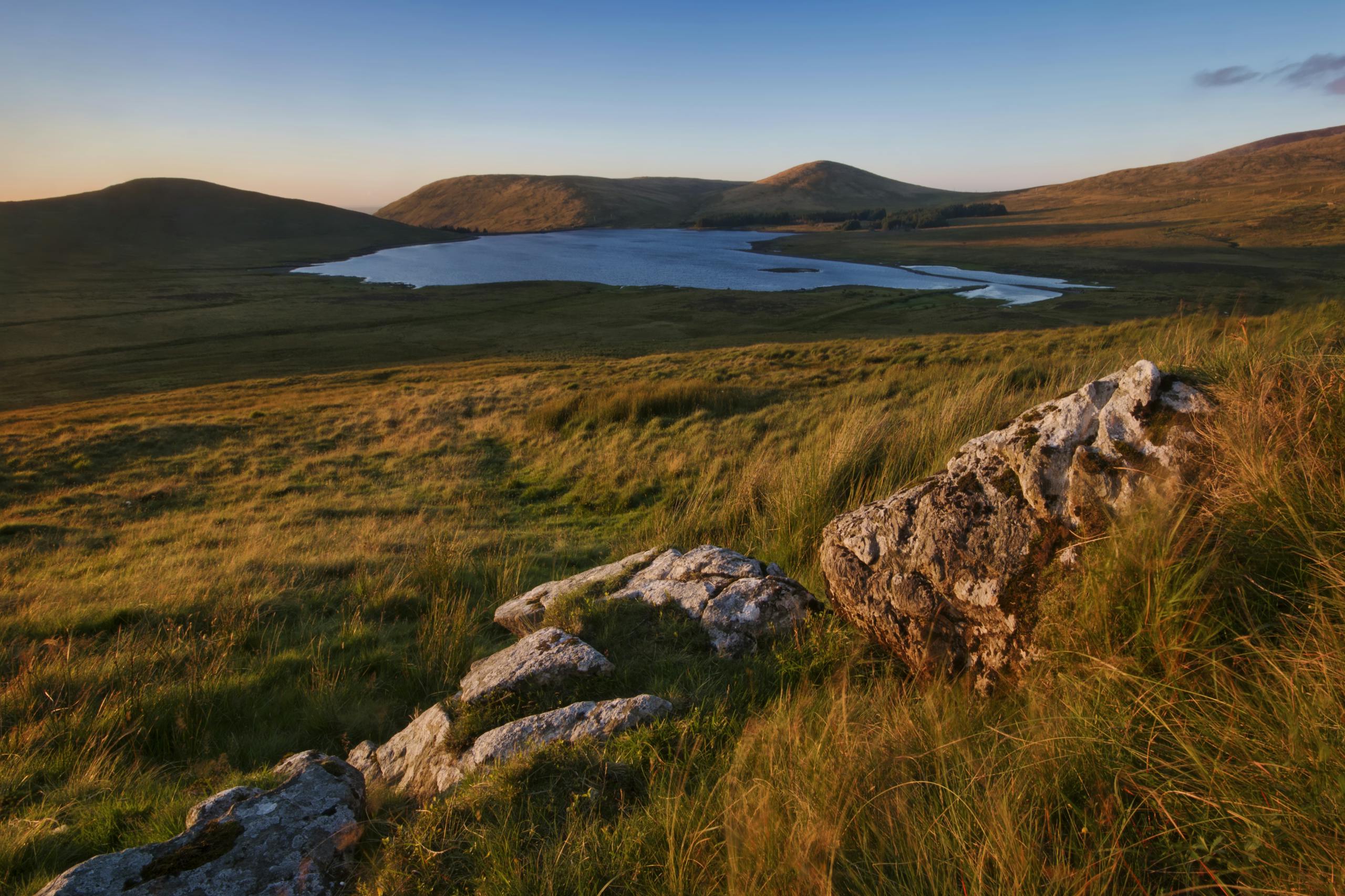Breathtaking view of Northern Ireland's landscape with lake, hills, and grassland at sunset.