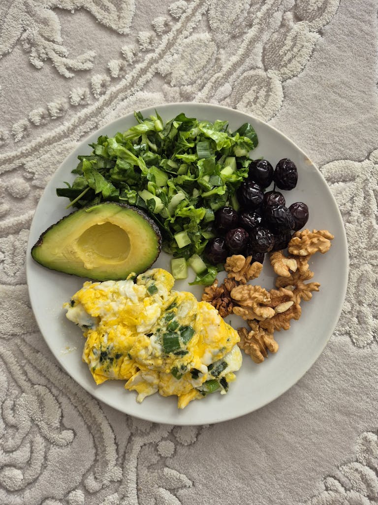 Delicious breakfast with eggs, avocado, greens, berries, and walnuts on a textured background.